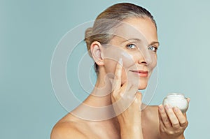 Mature woman applying skin cream on face photo