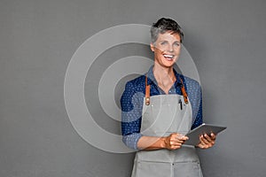 Mature woman in apron holding digital tablet