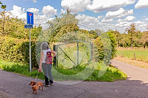 Mature woman with a backpack with her dog standing on a rural street looking at a sign indicating: this road is a dead end