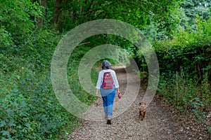 Mature woman with a backpack walking quietly with her dog on a rural path among trees