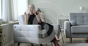 Mature woman blab on cellphone rest on armchair at home