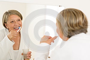Mature woman brushing teeth look bathroom mirror