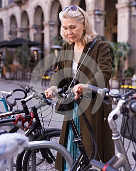 Mature woman chooses rental bike on city street