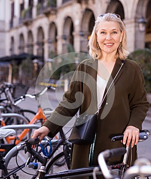 Mature woman chooses rental bike on city street