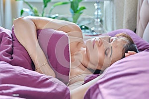 Mature woman with closed eyes sleeping in bed at home