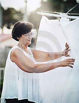 Mature woman, clothesline and laundry outdoor with household domestic chores, spring cleaning and housekeeping. Hanging