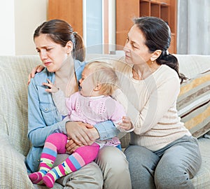 Mature woman comforting adult daughter with toddler