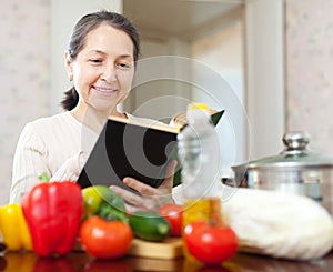 Mature woman cooking with cookbook