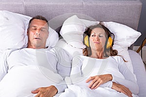 Woman Covering Her Ears With Headphones While Man Snoring photo