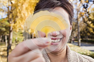 Mature Woman Covering Her Eyes with Yellow Ginkgo Leaf