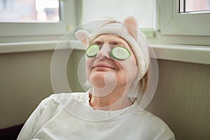 Mature woman covers eyes with cucumber and enjoys life at home, wellness and beauty care at any age
