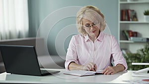 Mature woman creating shopping list, writing plans in notepad, busy housewife
