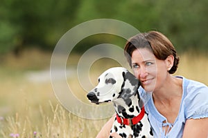 Mature woman is cuddling a dalmatian dog in a meadow outdoor