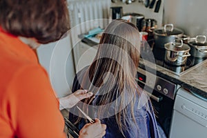 Mature woman cuts hair to young beautiful woman with long hair at home, because of quarantine