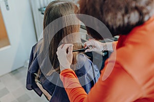 Mature woman cuts hair to young beautiful woman with long hair at home, because of quarantine