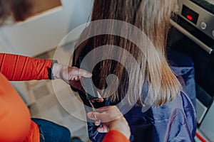 Mature woman cuts hair to young beautiful woman with long hair at home, because of quarantine