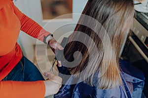 Mature woman cuts hair to young beautiful woman with long hair at home, because of quarantine