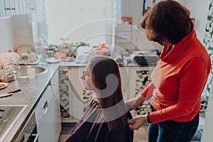 Mature woman cuts hair to young beautiful woman with long hair at home, because of quarantine