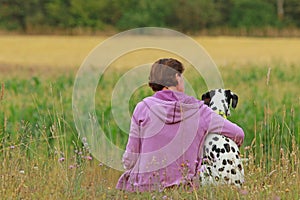 Mature woman and dalmatian dog from the back sitting in the mead