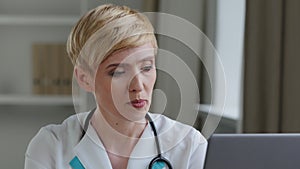 Mature woman doctor practitioner cardiologist pediatrician wears white medical gown and stethoscope sits in clinic uses