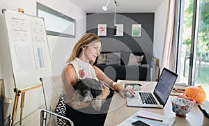 Mature woman with dog working indoors in home office in container house in backyard.