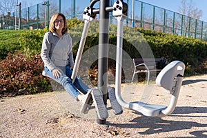 Mature woman doing exercises with her legs in a gymnastics apparatus in a public park.
