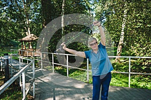 Mature woman doing exercises with Nordic walking poles in summer