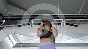 Mature woman is doing pull-ups with a narrow grip in gym. Sport concept.