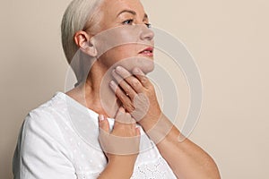 Mature woman doing thyroid self examination on beige background