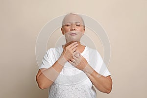 Mature woman doing thyroid self examination on beige background