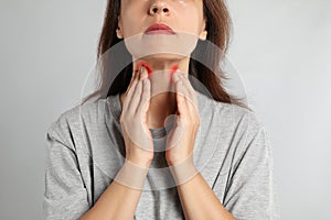 Mature woman doing thyroid self examination on light background, closeup