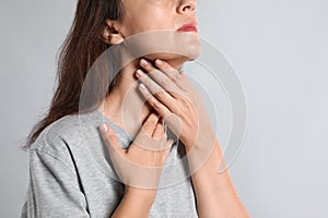 Mature woman doing thyroid self examination on light background, closeup
