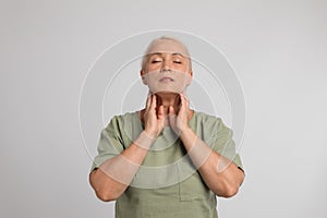 Mature woman doing thyroid self examination on light grey background