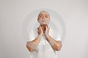 Mature woman doing thyroid self examination on light grey background