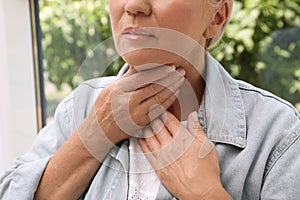 Mature woman doing thyroid self examination near window, closeup