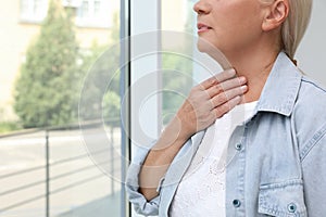 Mature woman doing thyroid self examination near window, closeup. Space for text