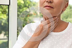 Mature woman doing thyroid self examination near window, closeup. Space for text