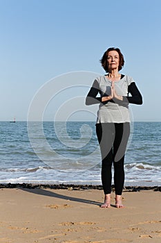 Mature woman doing yoga on the beach