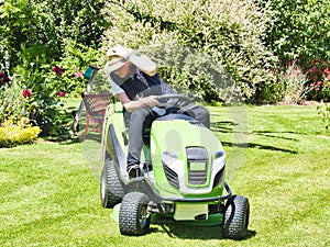 Mature woman driving a tractor lawn mower in garden with flowers