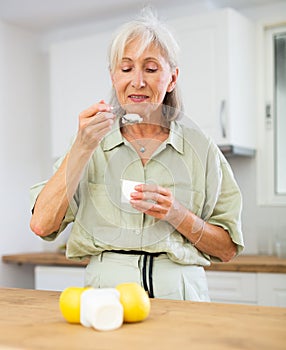 Mature woman eating tasty yogurt in kitchen