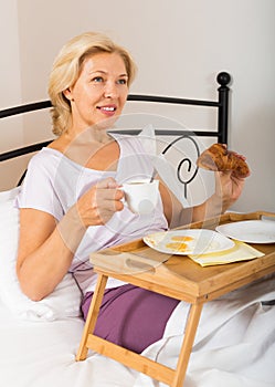 Mature woman enjoying breakfast in bed