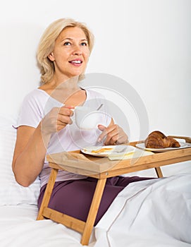 Mature woman enjoying breakfast in bed