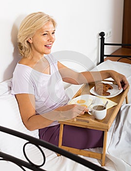 Mature woman enjoying breakfast in bed