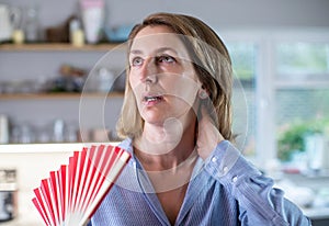 Mature Woman Experiencing Hot Flush From Menopause Using Fan