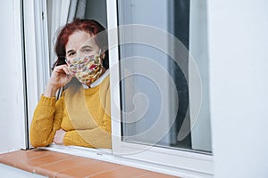 Mature woman with face mask on window