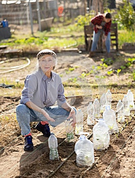 Mature woman farmer sets up plastic bottles to protect plants from harmful insects