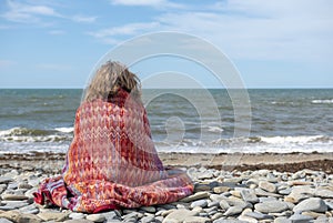 Mature woman in fifties sitting on a rocky beach lookingout