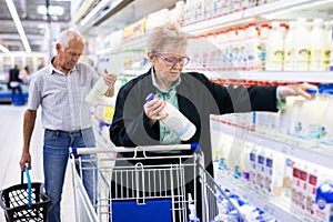Mature woman with glasses chooses milk in the dairy section of supermarket