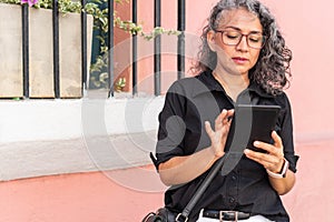 Mature woman in glasses holds tablet outdoors