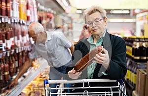 Mature woman with glasses picks out salami in the meat section of the supermarket